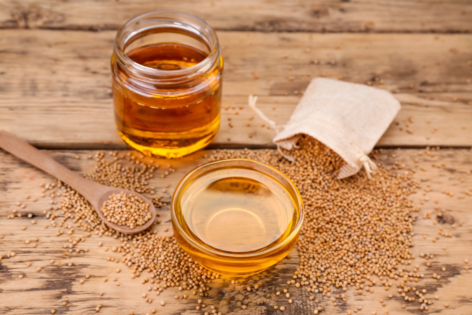Natural oil and mustard seeds on wooden table